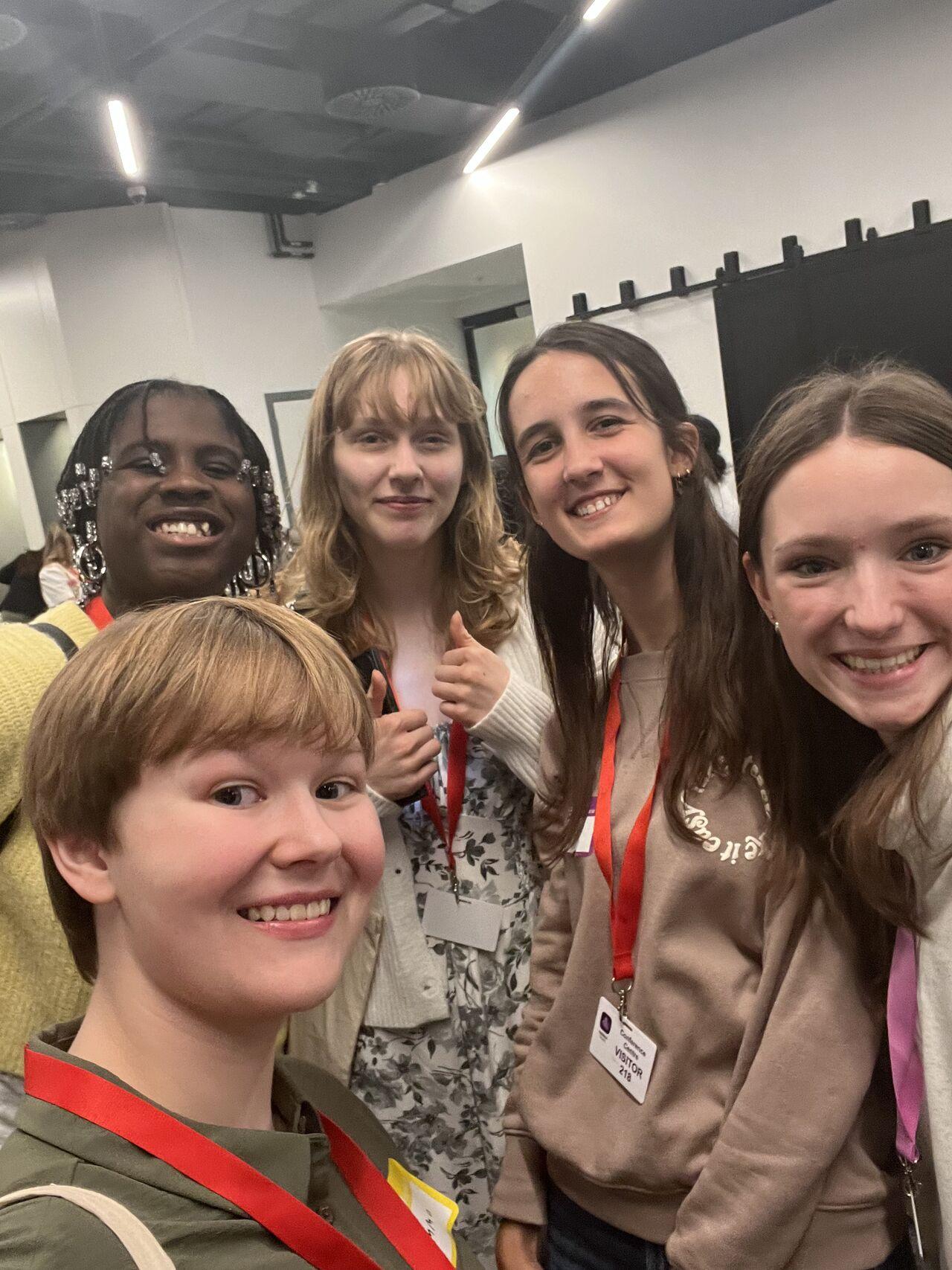 Five young women smiling for a selfie at Next Tech Fest, with one participant giving a thumbs up.