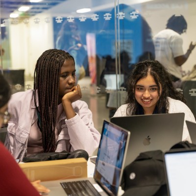 Two teenage girls sit and look at a laptop together during a workshop at Next Tech Fest