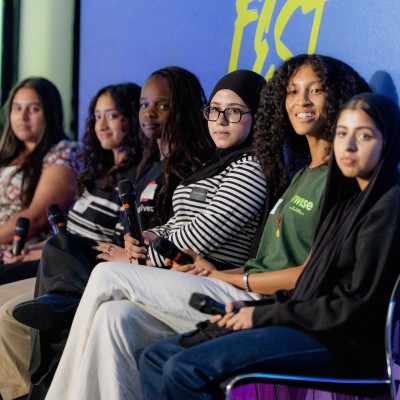 Six diverse young women sit on stage at Next Tech Fest