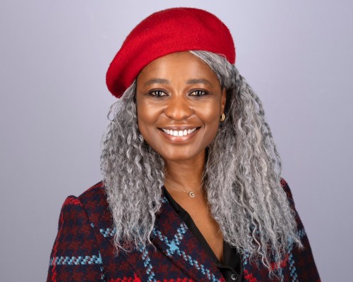 A black woman with curly silver hair wearing a bright red beret is looking directly at the screen with a big smile.
